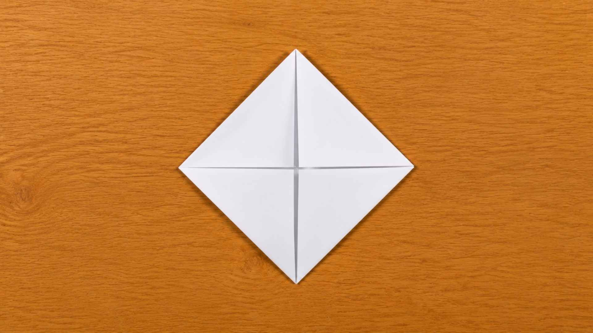 White origami paper folded into a diamond shape placed on a wooden table with soft natural lighting and shadows.