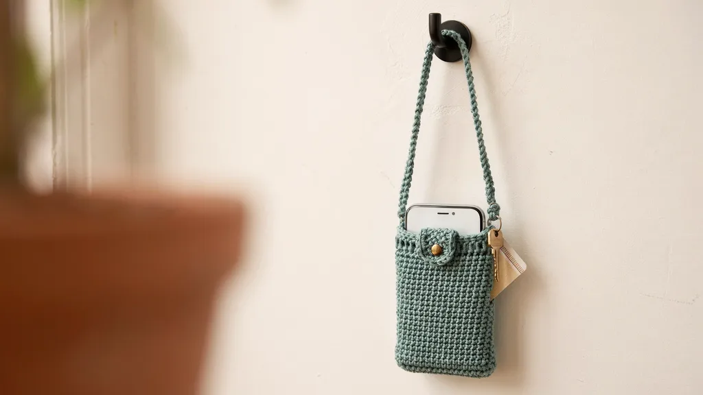 Slim crochet phone bag worn hung on a hook with a phone peeking out.
