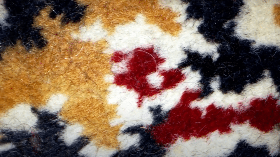 A multi-colored patterned outdoor rug featuring a bold, abstract camouflage-like design in shades of orange, dark red, navy blue, and white.