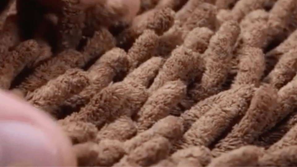 A close-up of thick, brown textured loop pile or shag outdoor carpet fibers.