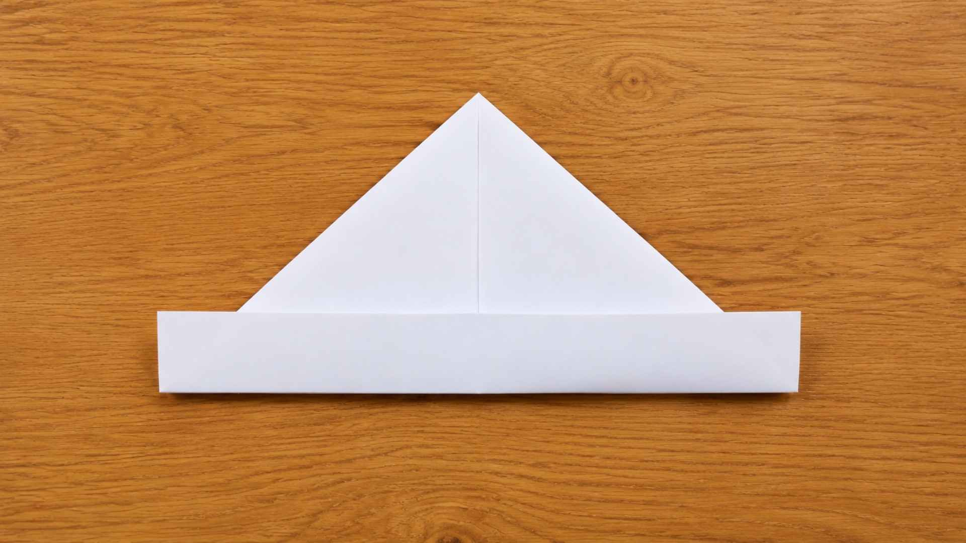 White origami paper shaped into a simple folded hat on a warm wooden table with soft natural lighting.