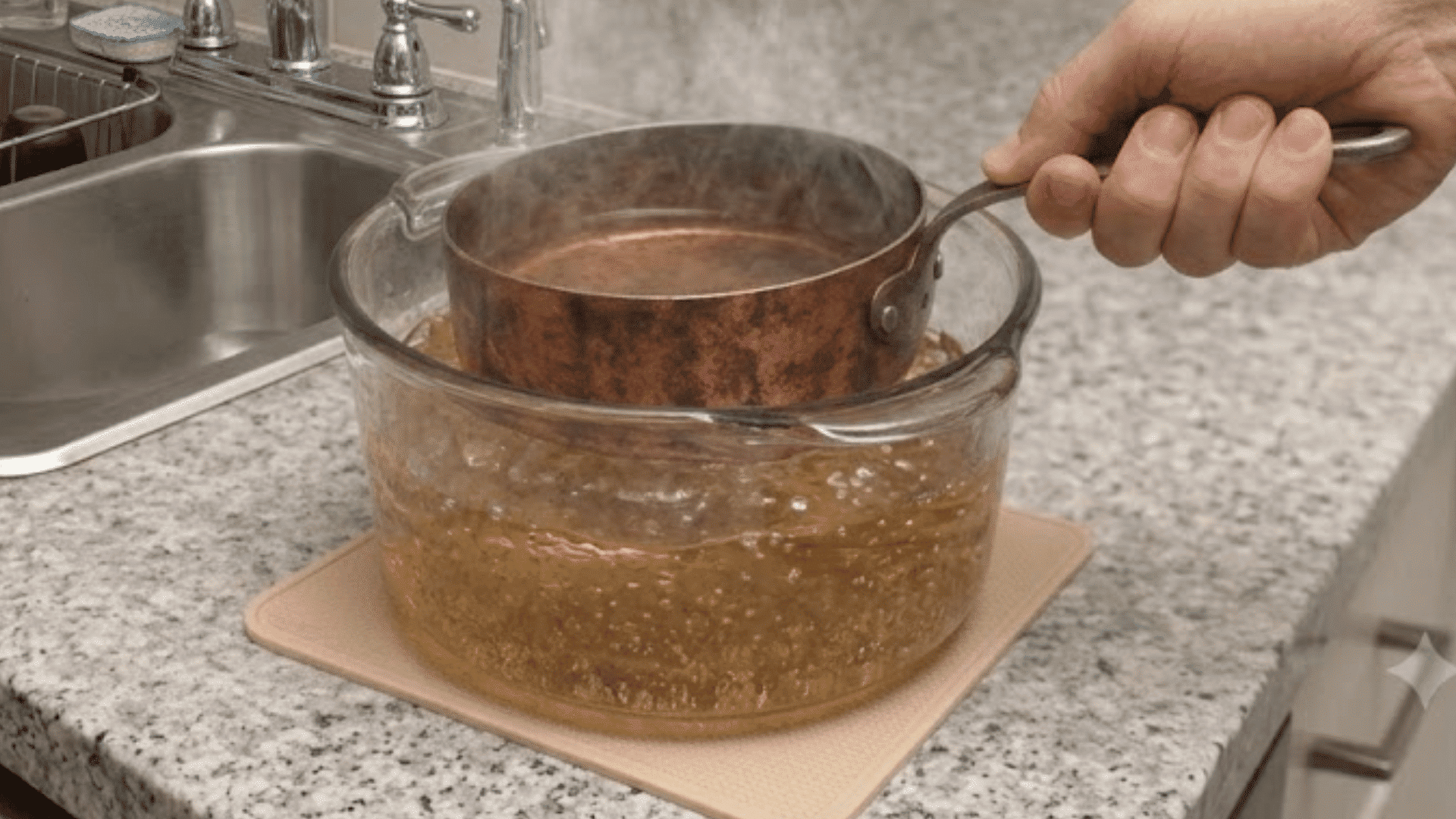 Copper pan soaking in water inside a glass bowl on a kitchen counter
