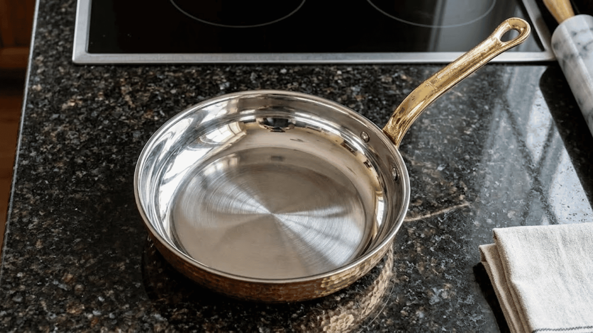 Stainless steel copper pan with brass handle on a dark kitchen countertop
