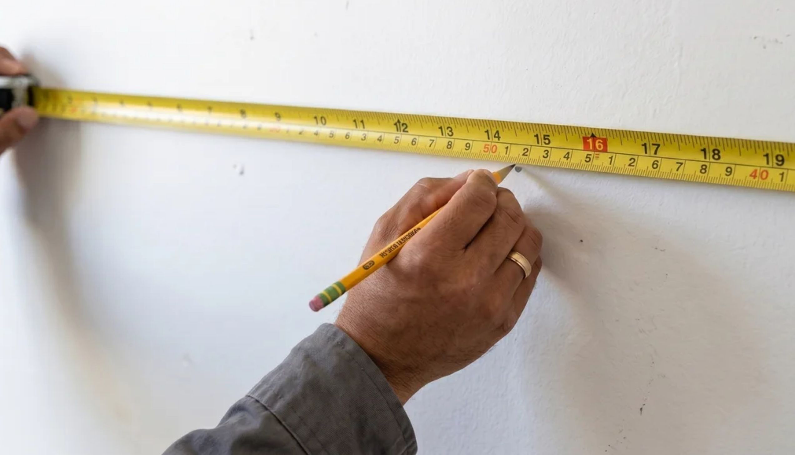 Hand marking the wall with a pencil and measuring tape to find the correct hanging position for a mirror