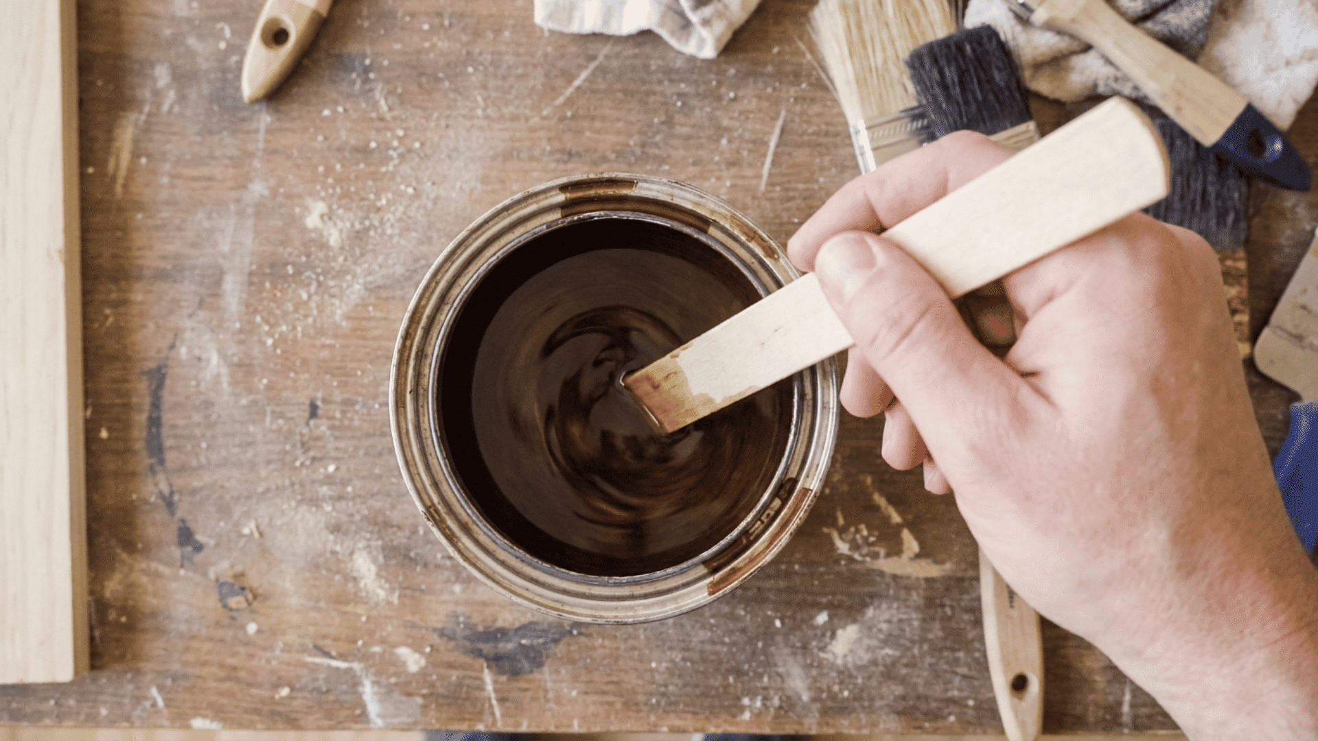 Wood stain being stirred slowly in a can with a wooden stick on a workshop bench
