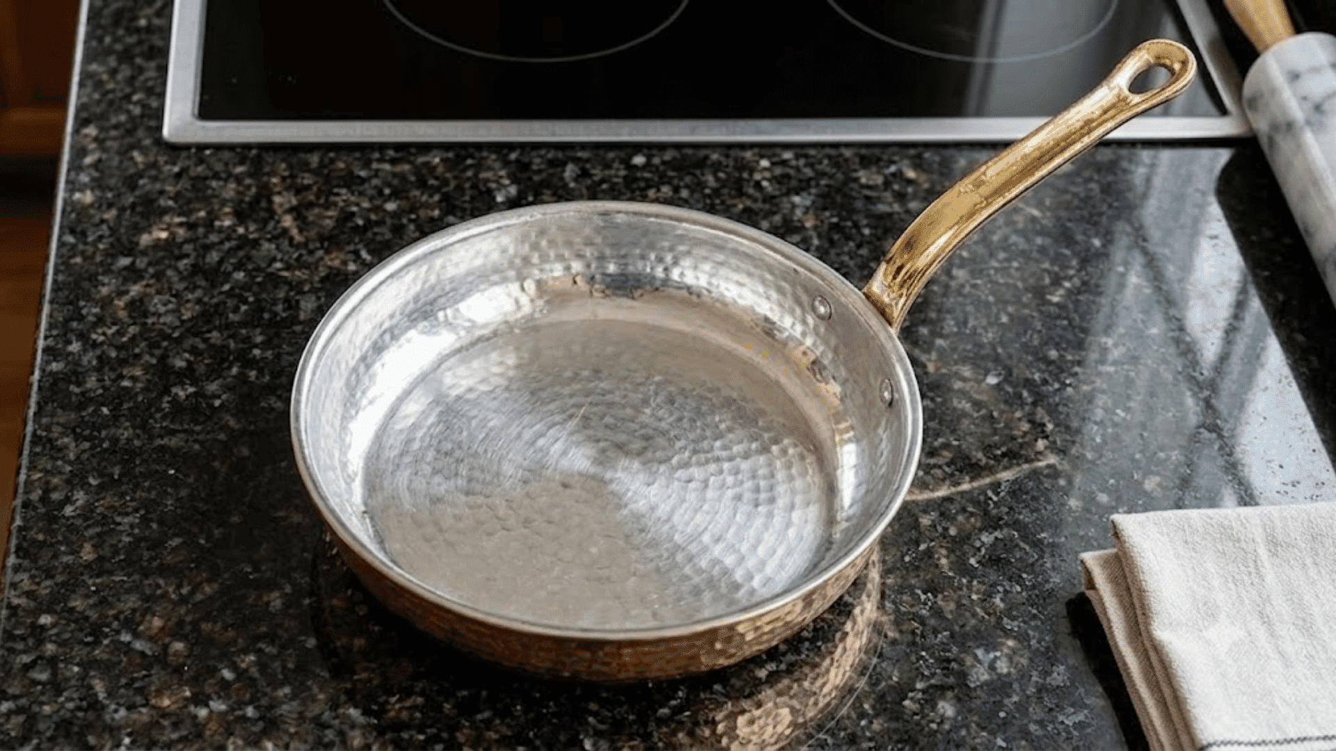 Tin-lined copper pan on a dark kitchen countertop with a brass handle