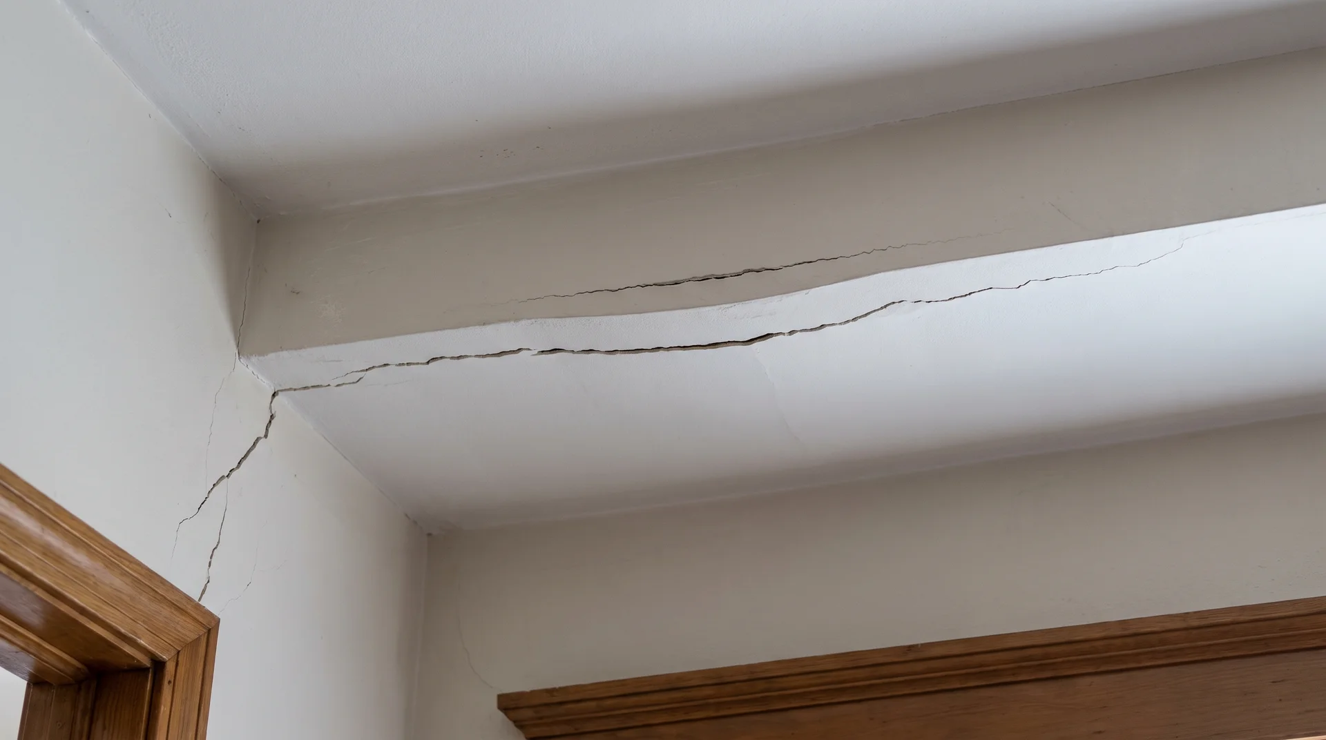 Sagging ceiling with long drywall crack and diagonal stress crack at wall corner showing structural load redistribution damage.