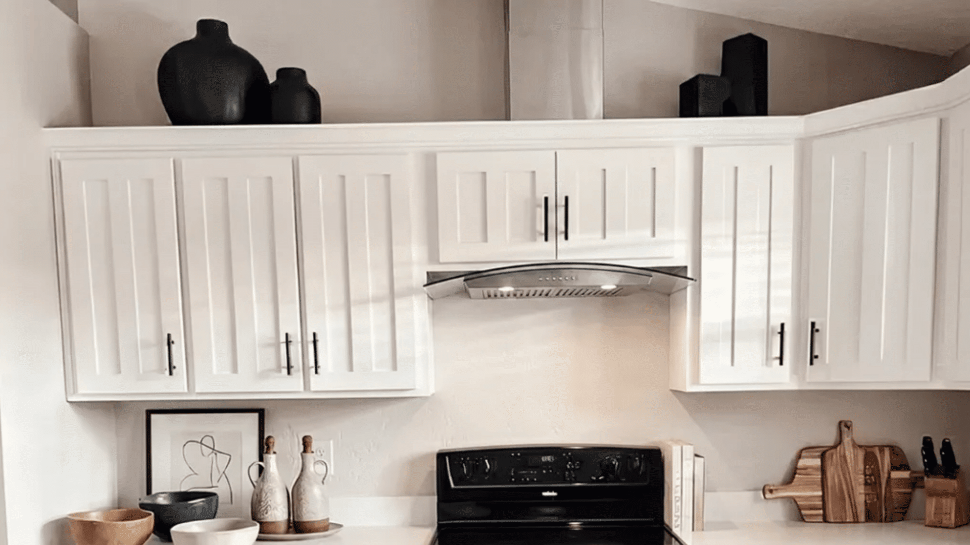White kitchen with upper cabinets, black stove, and decorative vases and wooden accents displayed above and on the counter.