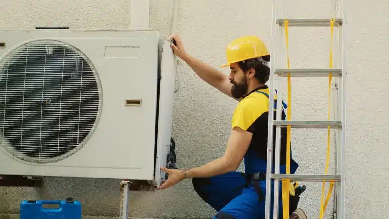 Technician in yellow hard hat installing outdoor air conditioning unit next to ladder