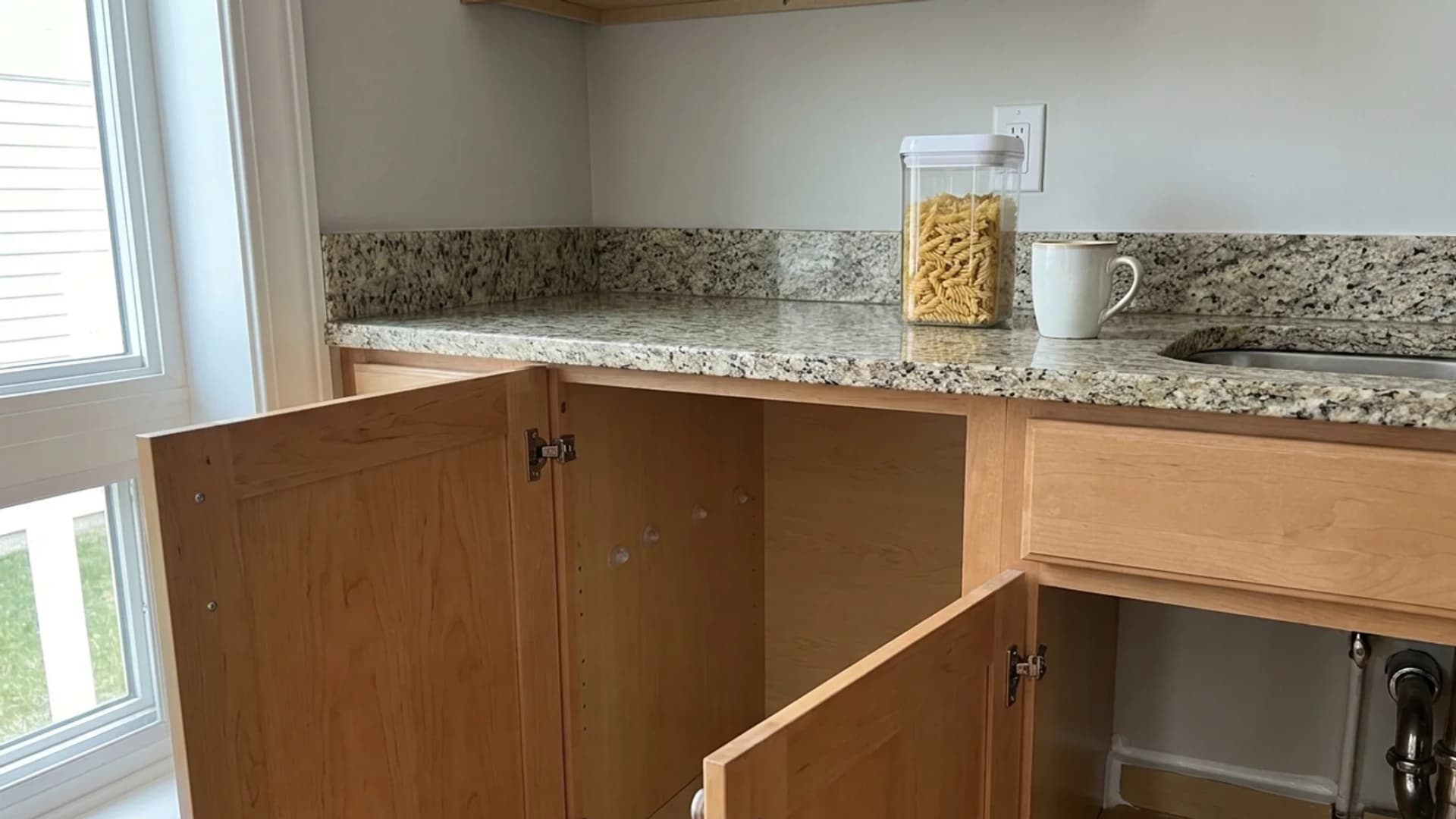 A tidy kitchen counter with open cabinet doors below, showing clear storage containers and clean surfaces near the sink.