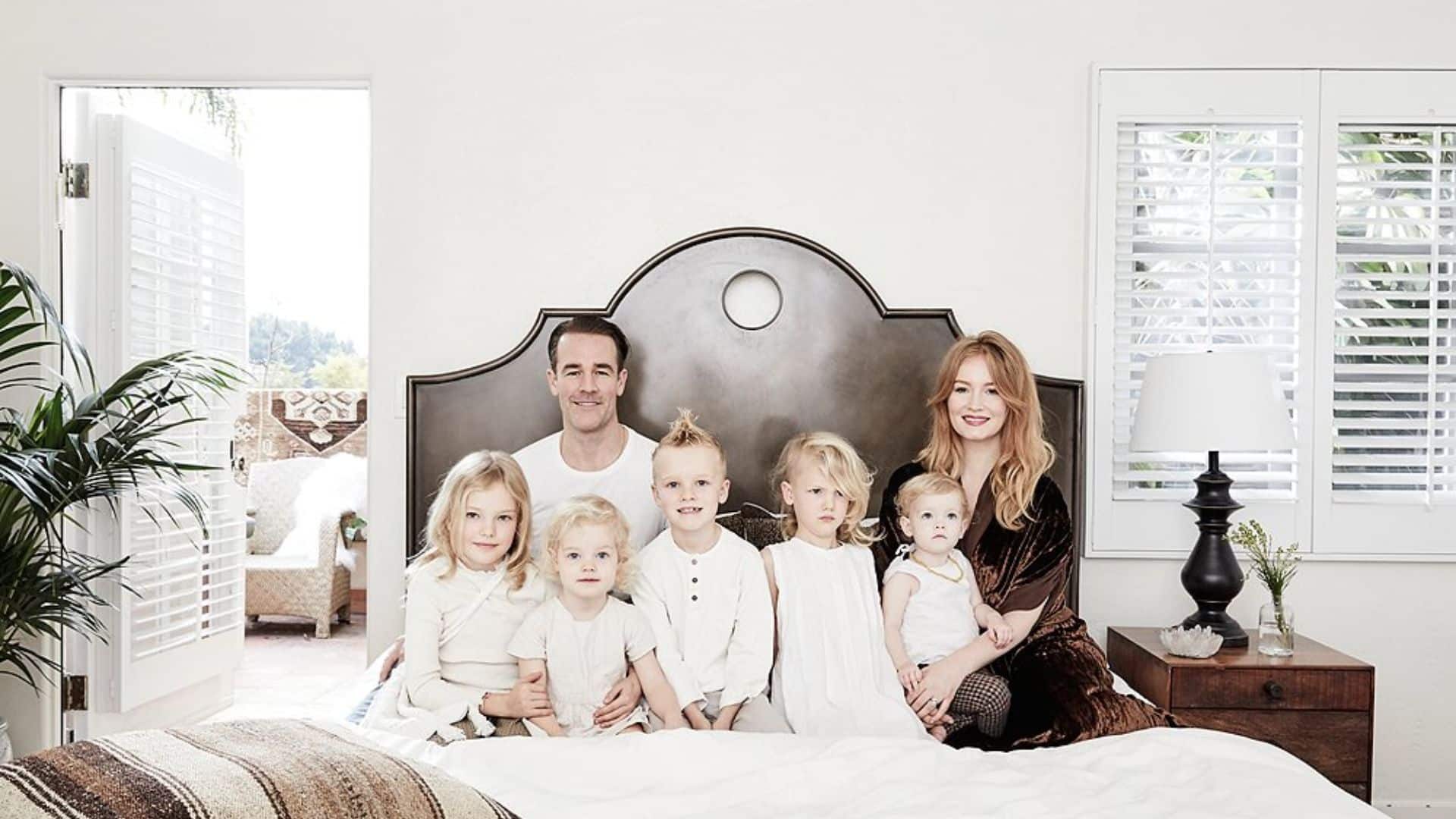 Actor and his wife posing with their children on a bed in a bright family portrait.