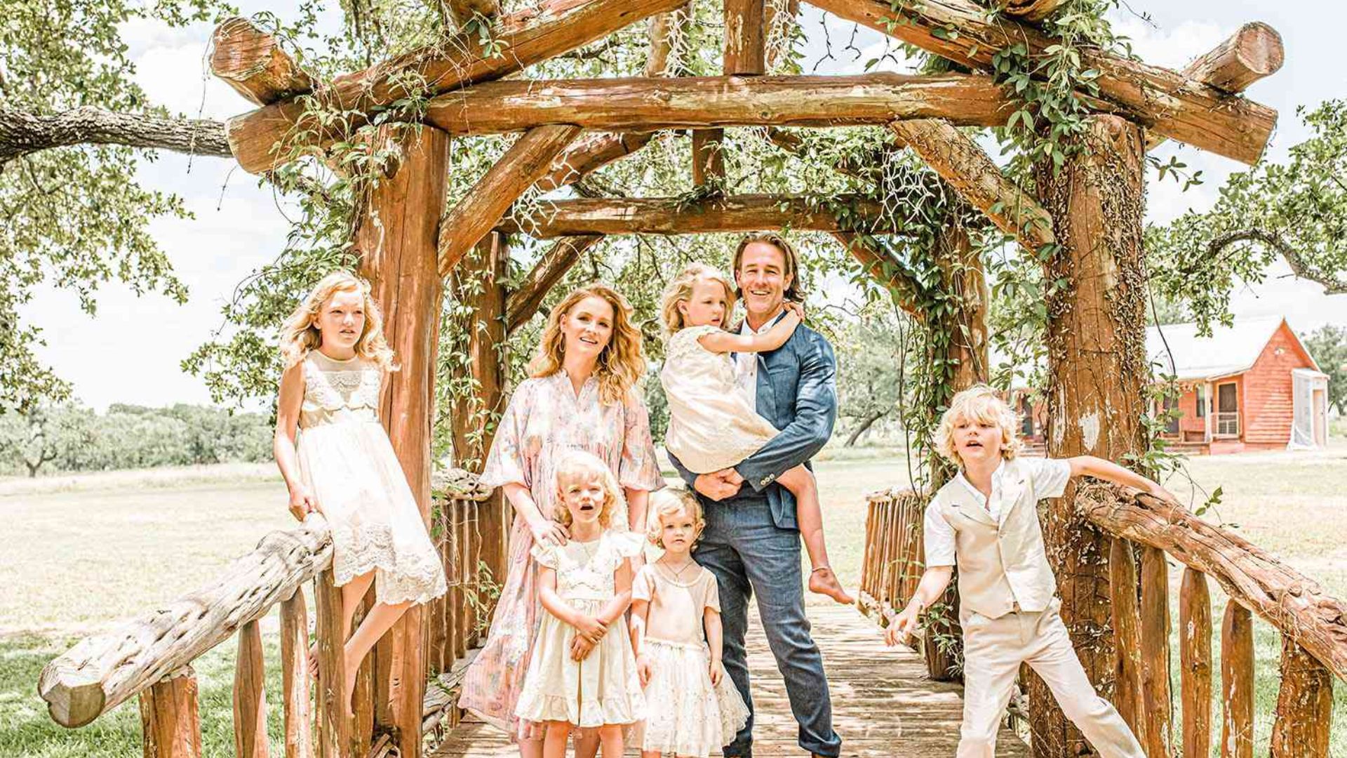 Actor posing with his wife and children outdoors beneath a rustic wooden structure.