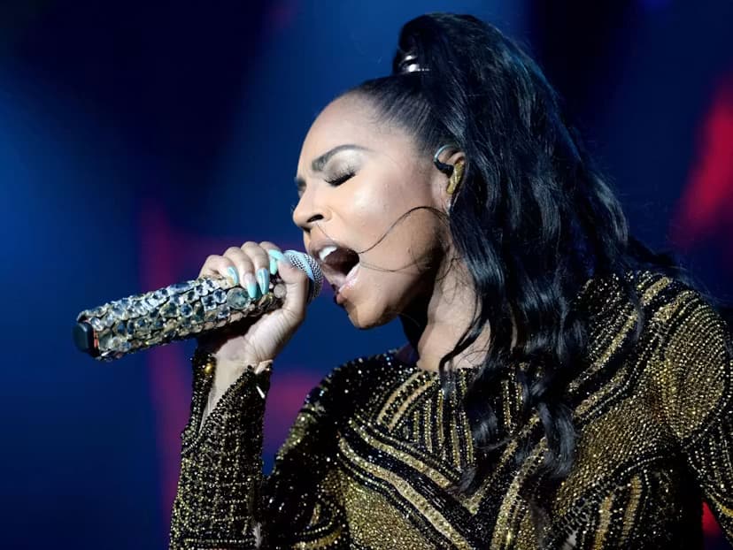Ashanti sings into a jeweled microphone on stage while wearing a black-and-gold embellished outfit.