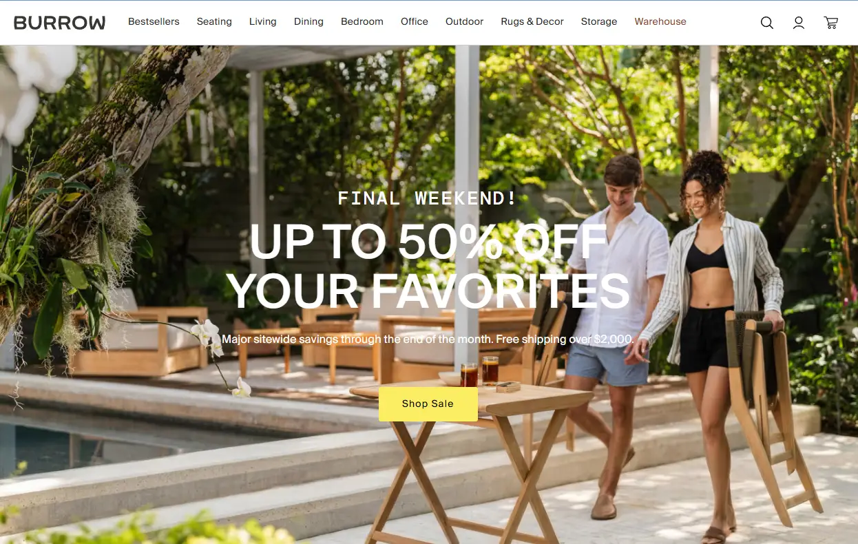 Couple carrying chairs outdoors by a poolside with wooden patio furniture