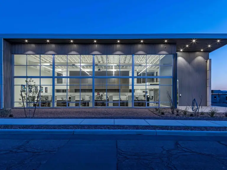 Modern office building with large glass windows illuminated at dusk, showcasing interior workspaces
