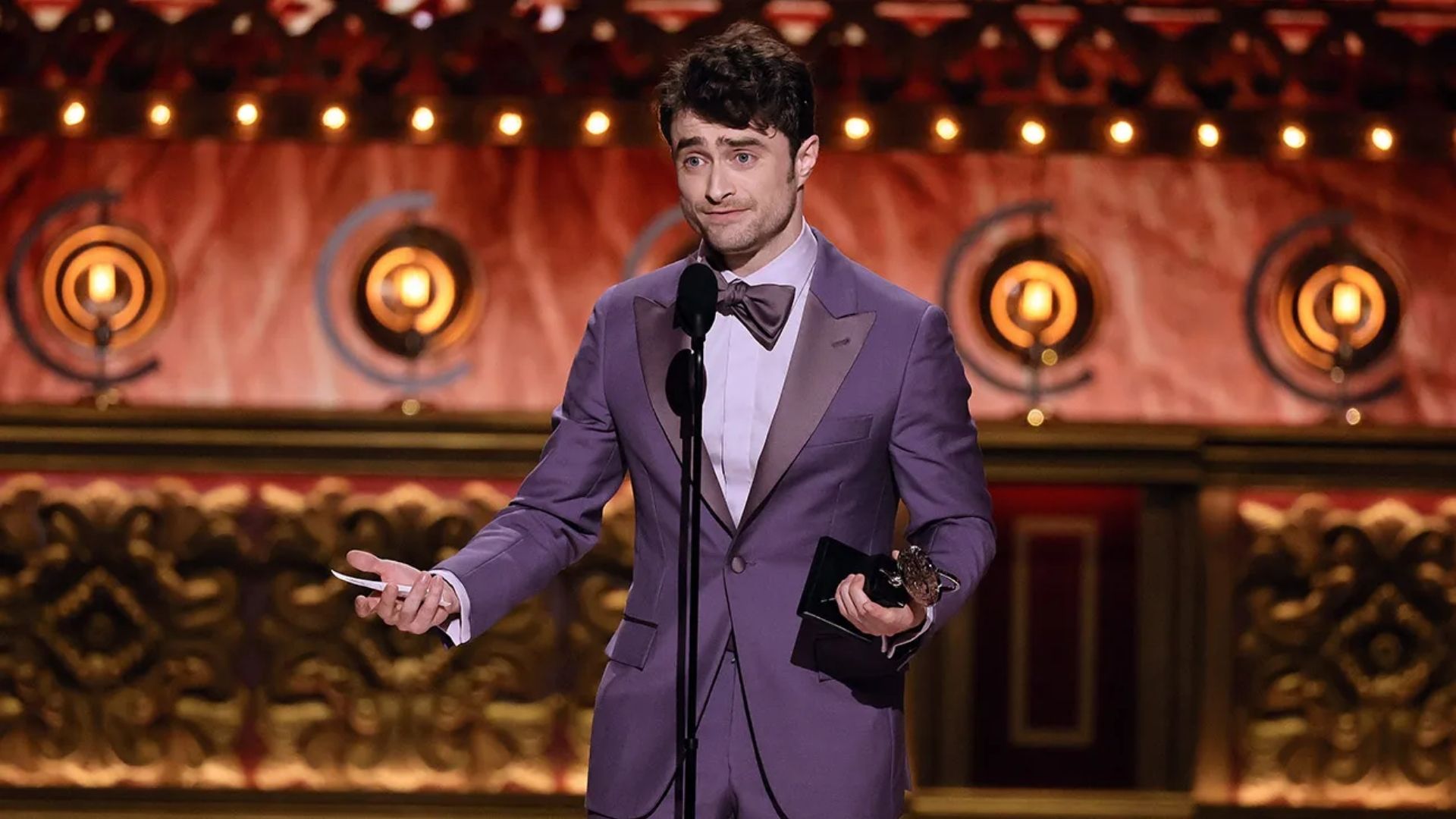 Daniel Radcliffe holding an award and speaking onstage at the Tony Awards.