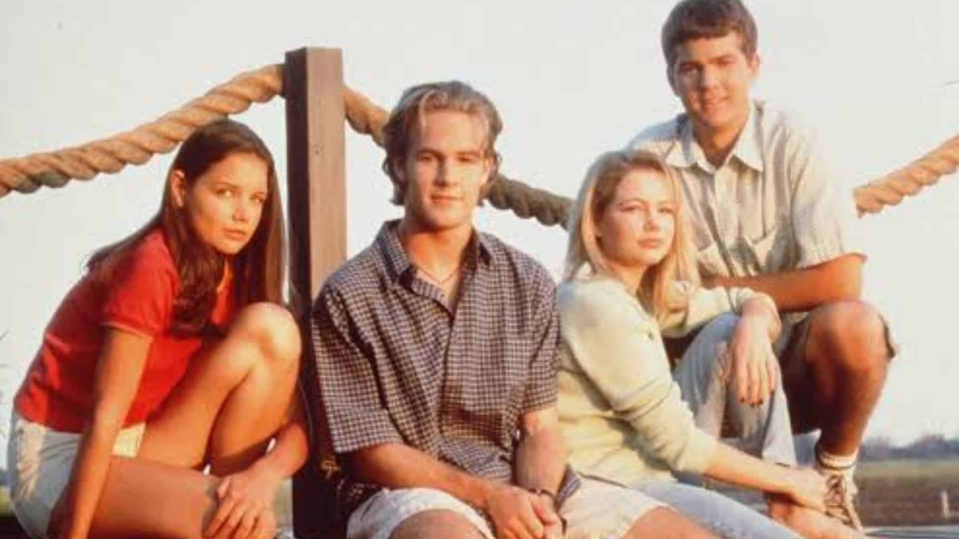 Four young television cast members posing together outdoors beside a wooden railing.