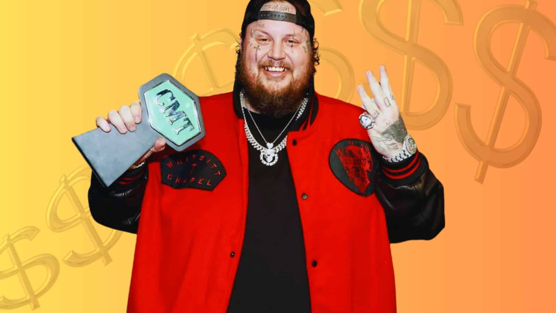 Jelly Roll holding an award while wearing a red jacket against a yellow background.