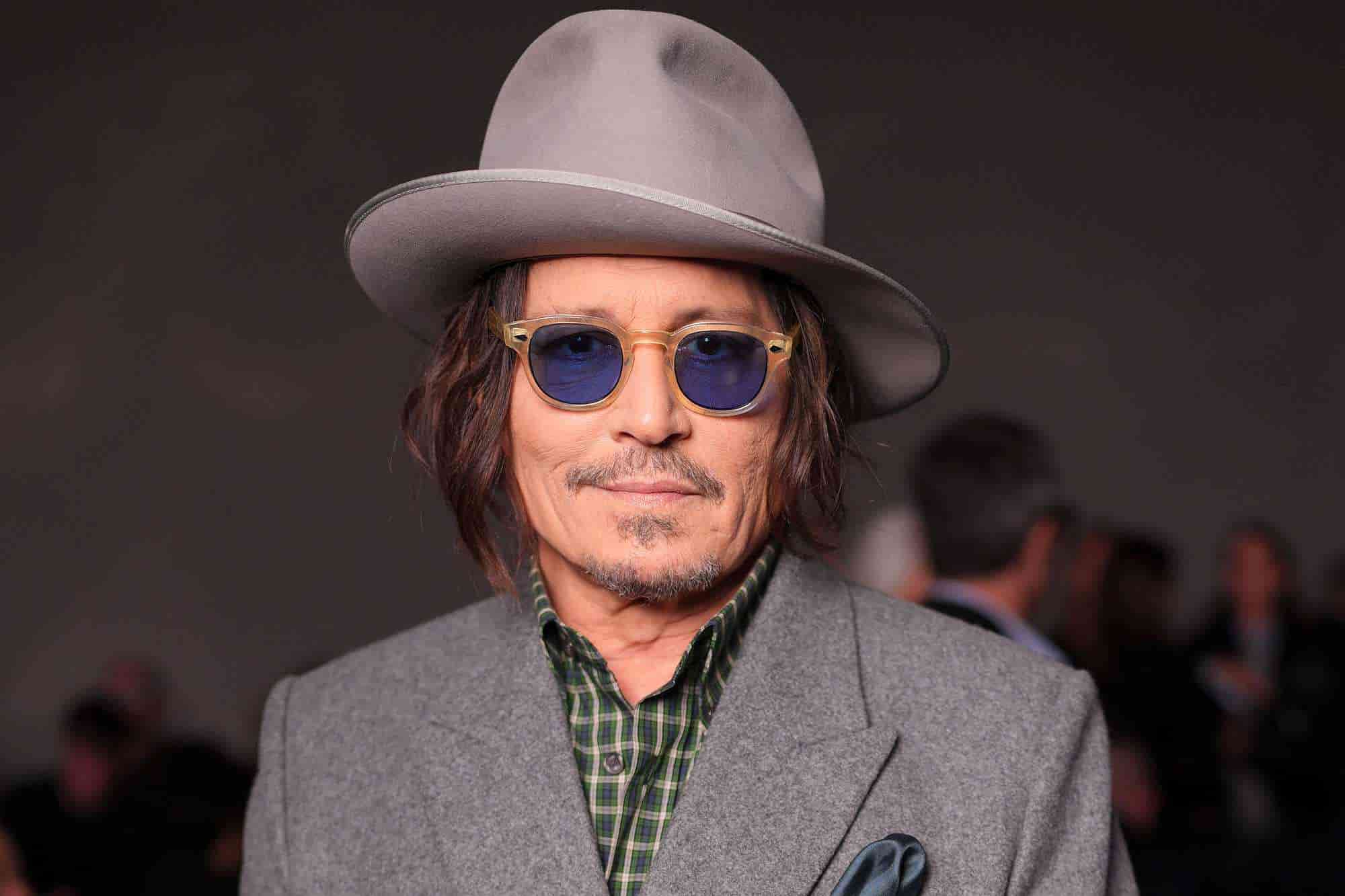 Johnny Depp wearing a gray hat, blue sunglasses, and gray suit at a public event