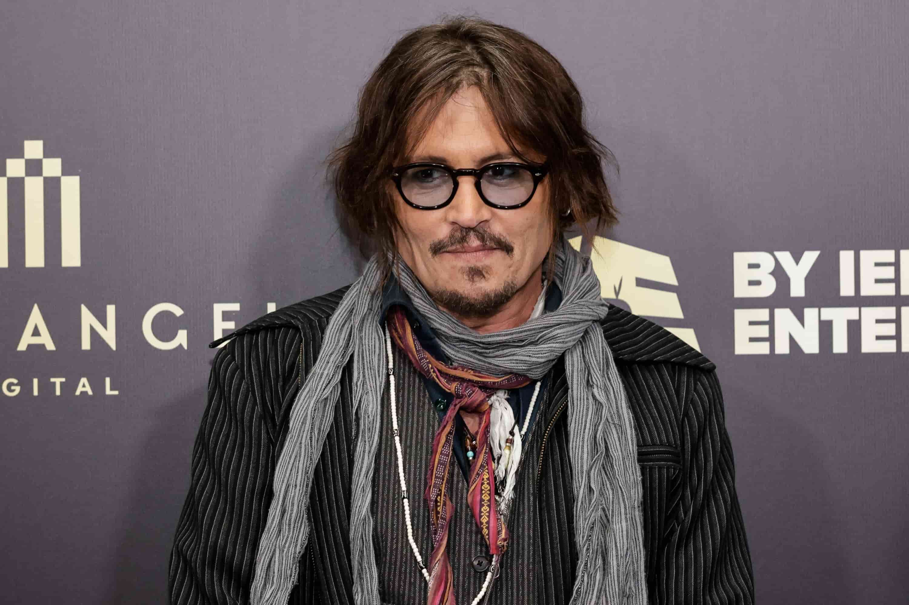 Johnny Depp wearing glasses, a scarf, and a black jacket at a public event backdrop