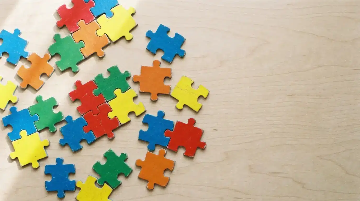 Scattered colorful puzzle pieces on light wooden table surface