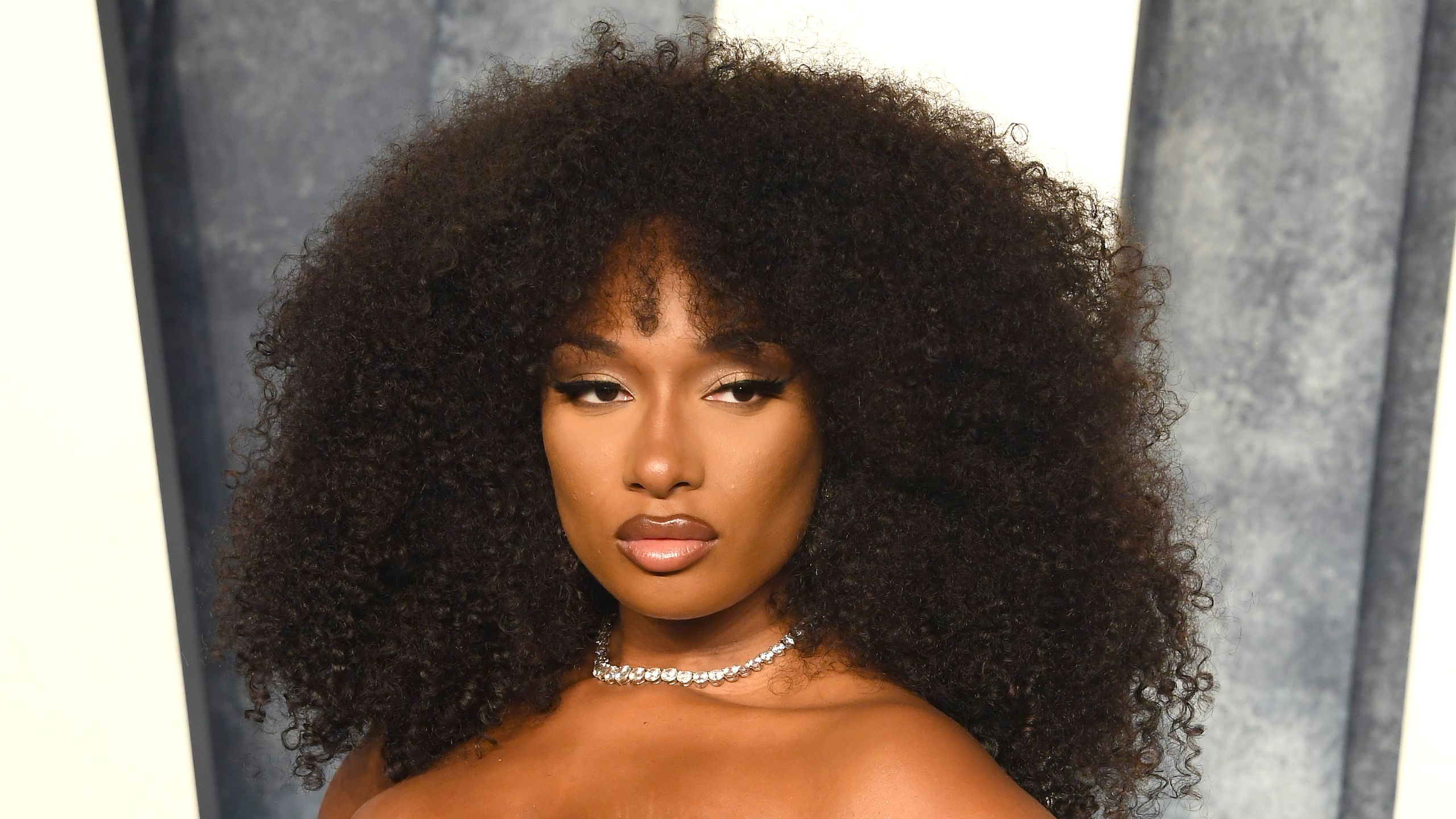 Megan Thee Stallion posing with natural curly hair at a red carpet event