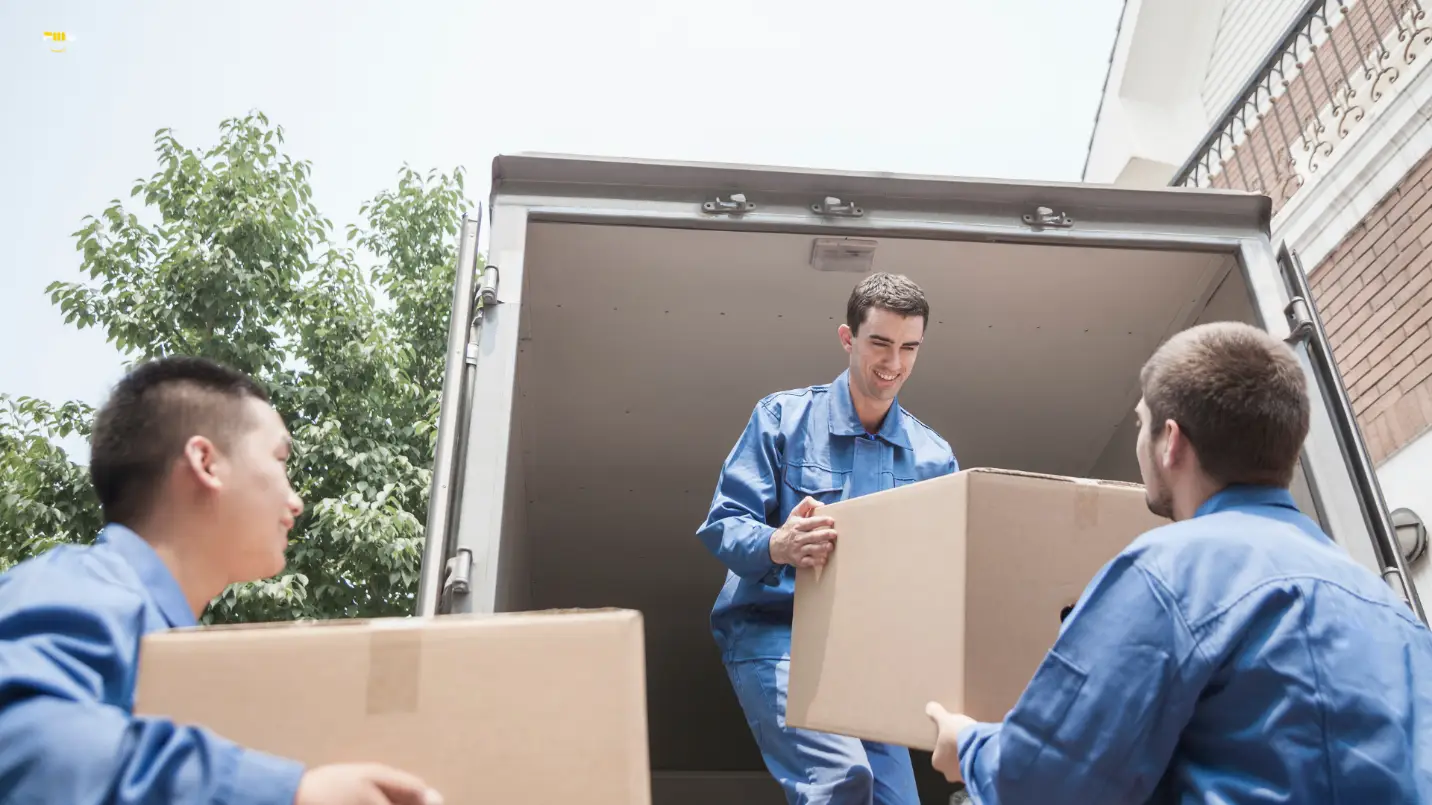Three workers in blue uniforms loading boxes into a moving truck outdoors