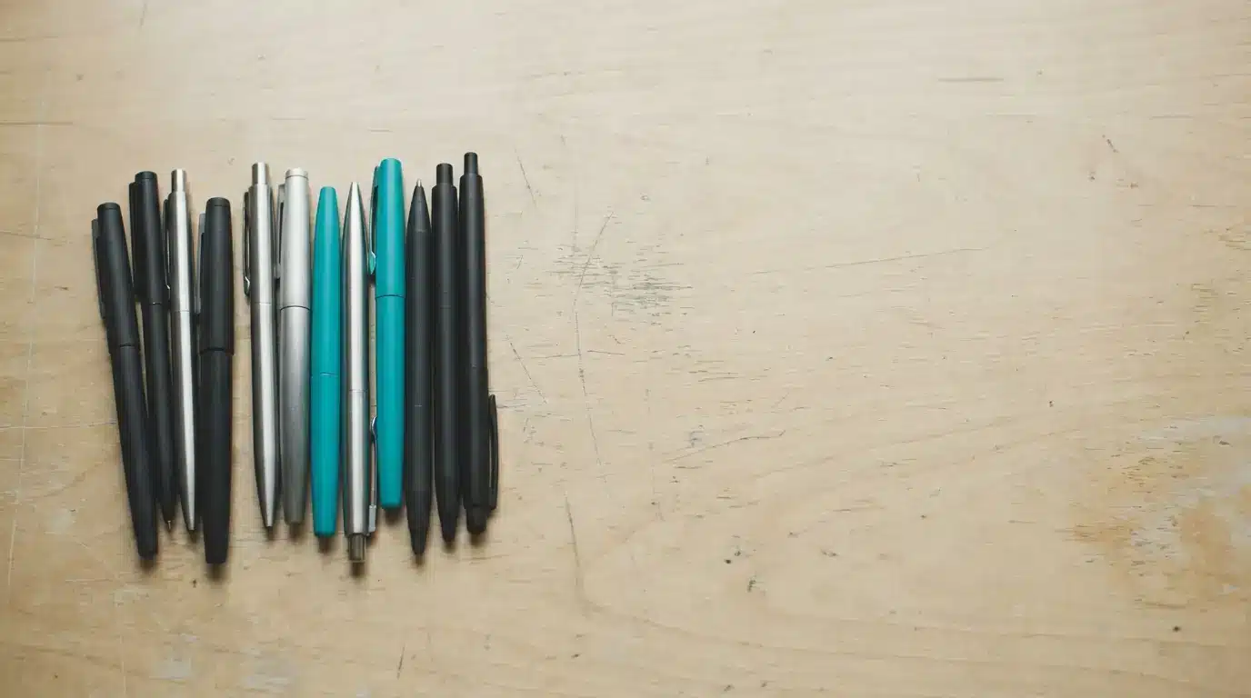 Pens of various colors arranged on a wooden surface in natural light
