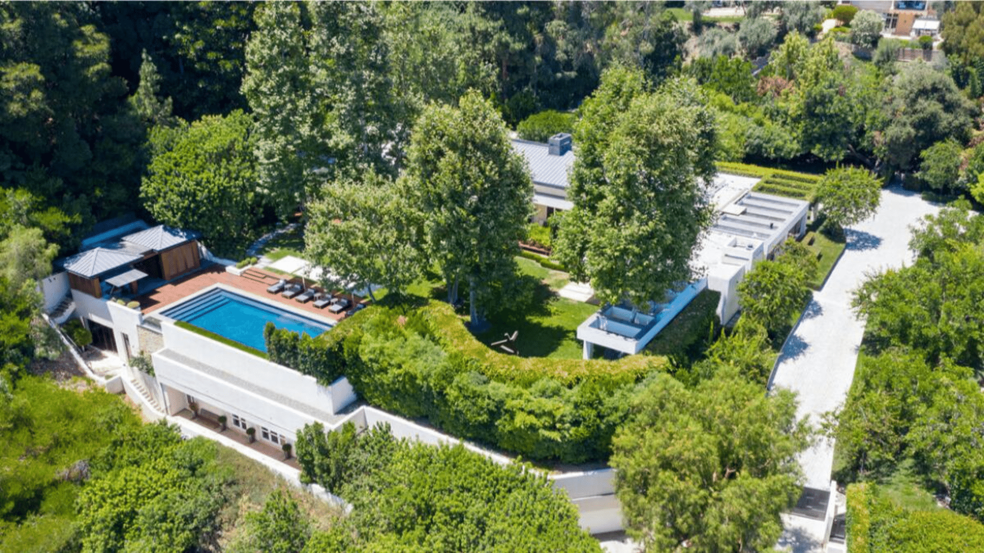 Aerial view of a luxury Beverly Hills mansion with a swimming pool, landscaped gardens, and private outdoor spaces.