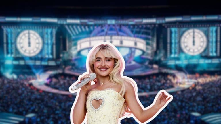 Sabrina Carpenter performing on stage in a white outfit during a concert with a large arena background.