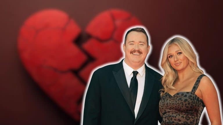 Shane Gillis posing with a blonde woman in front of a broken heart background.