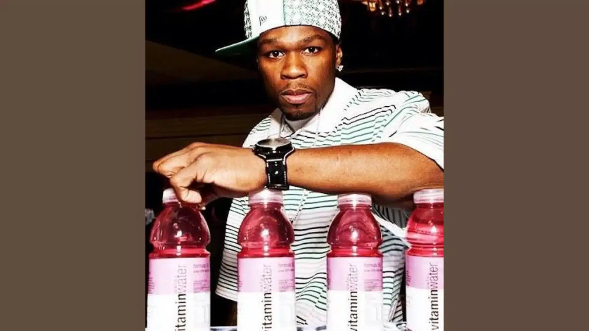 50 Cent standing behind several bottles of Vitaminwater, wearing a striped shirt and a hat