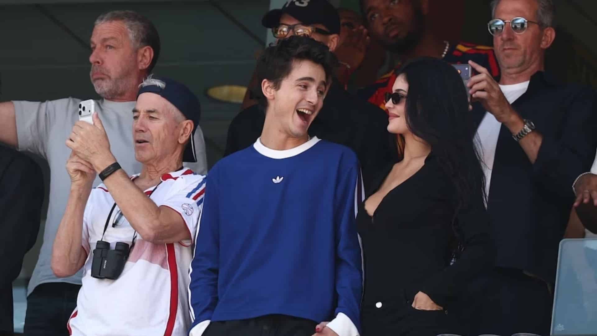 Timothée Chalamet and Kylie Jenner smiling together at a sporting event.