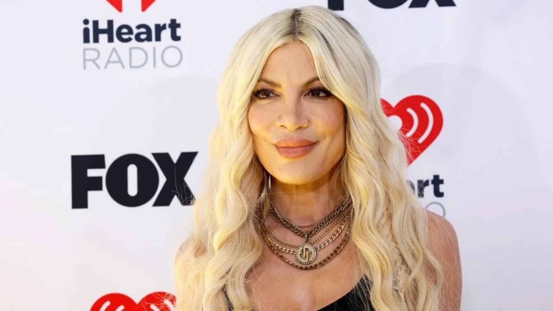 Tori Spelling attending an event with blonde hair and black outfit on red carpet background