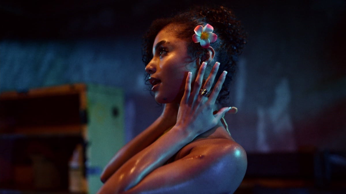 Tyla posing in profile with warm lighting and a flower in her hair against a blue background.