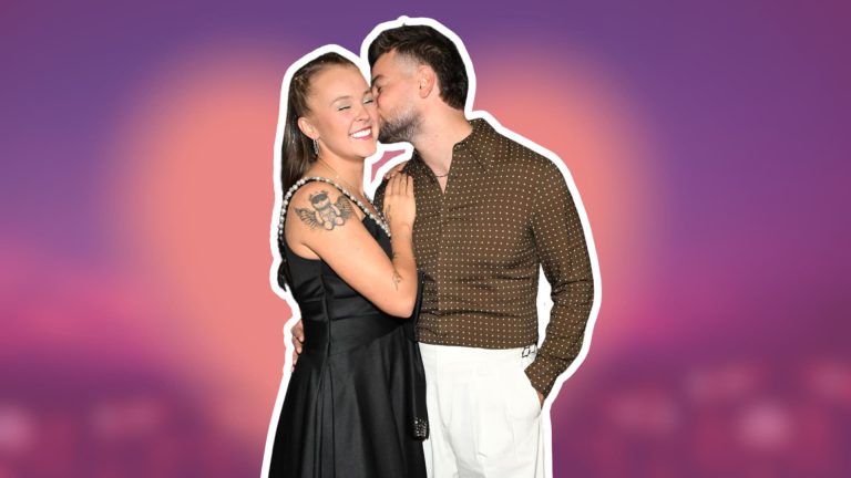 Jojo Siwa in a black dress smiles as her partner Chris Hughes kisses her cheek against a purple and pink background.