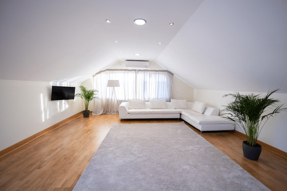 Bright attic living room with white sectional sofa, large window, wooden floor, and potted plants