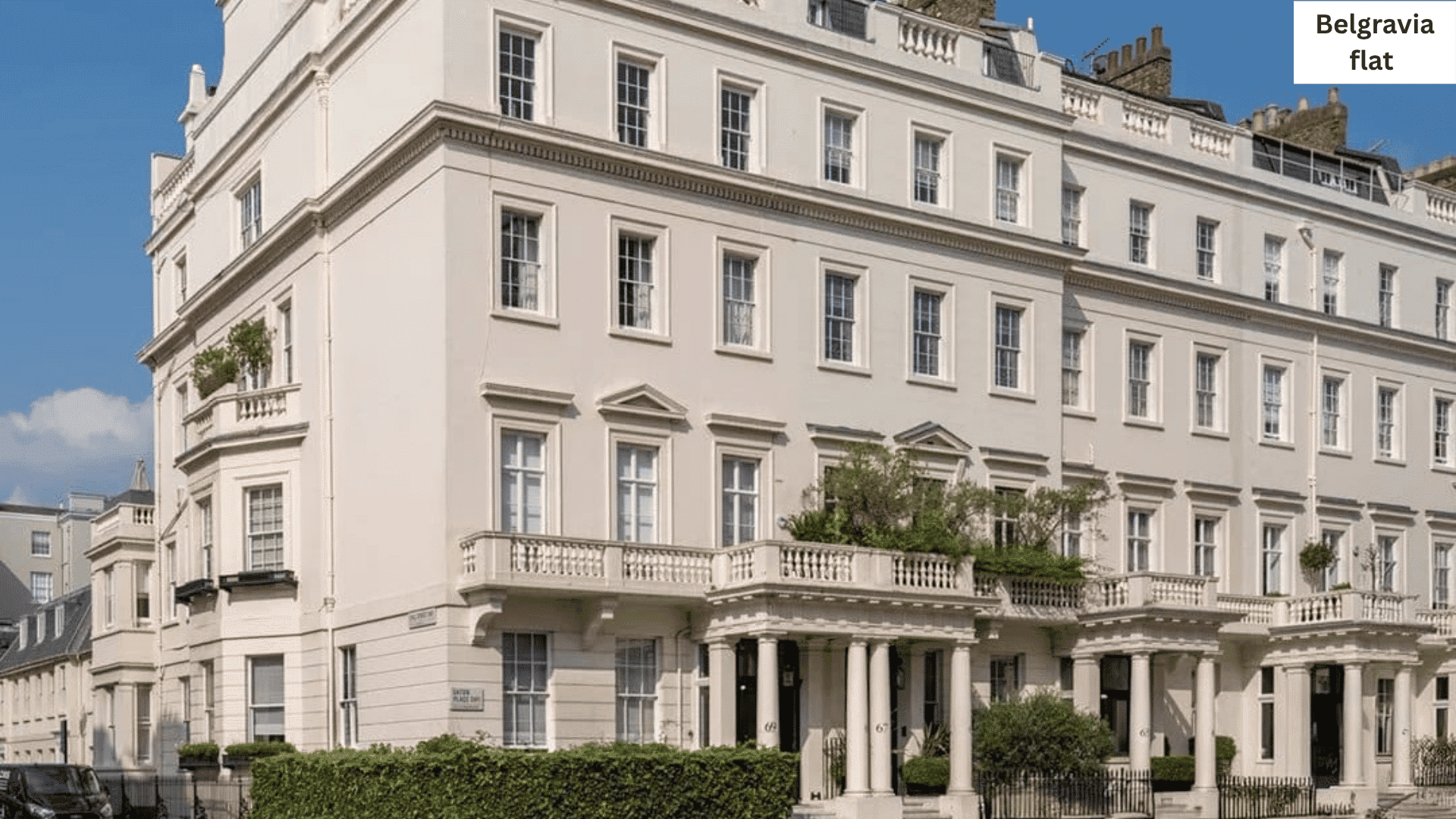 Exterior view of a grand, multi-story white neoclassical building with grand columns and decorative balconies against a clear blue sky.