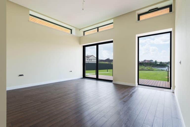 Empty modern room with dark wood flooring and large windows overlooking garden and pond