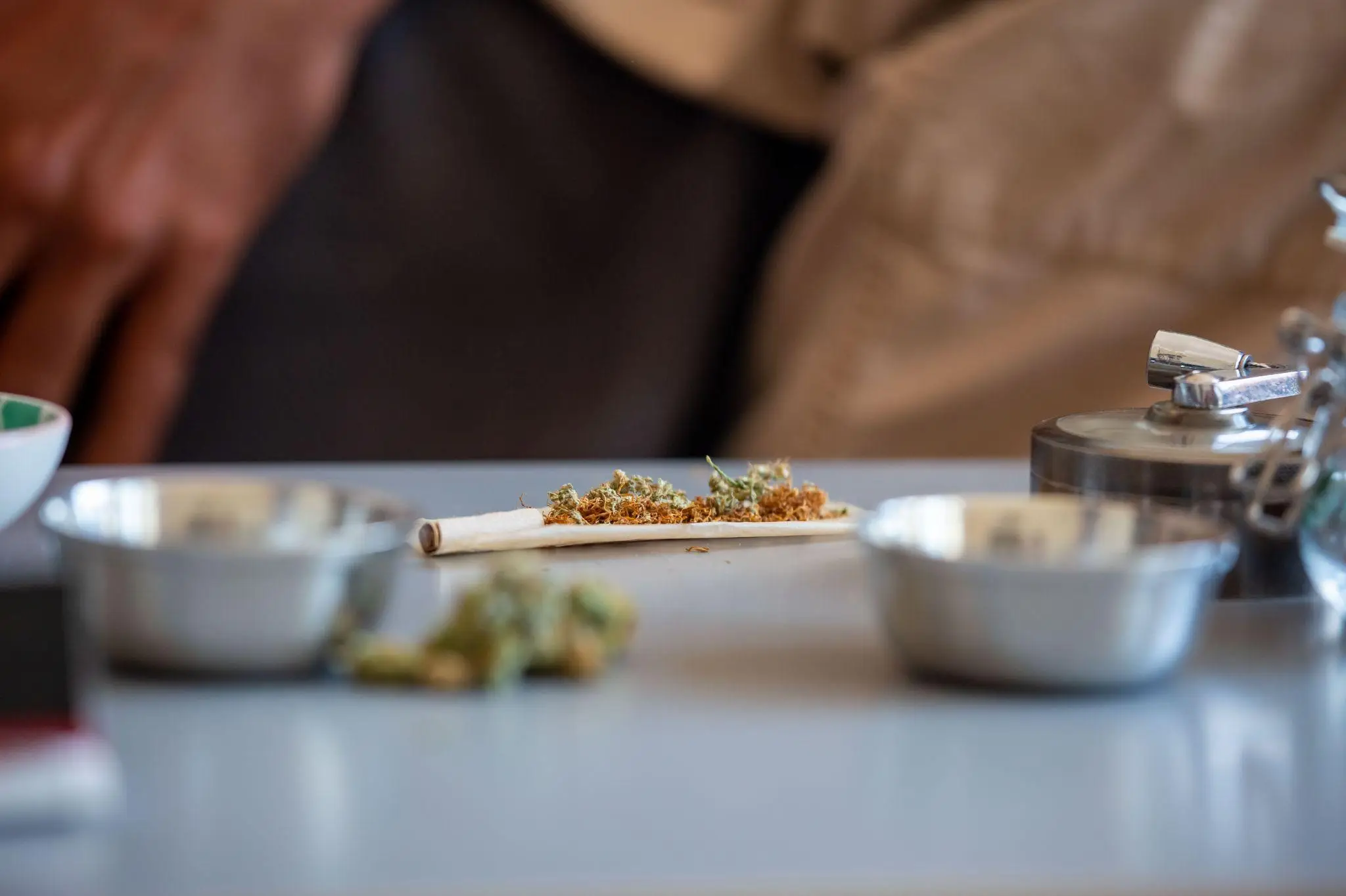 Rolling a cannabis joint on a table with metal bowls and grinder nearby