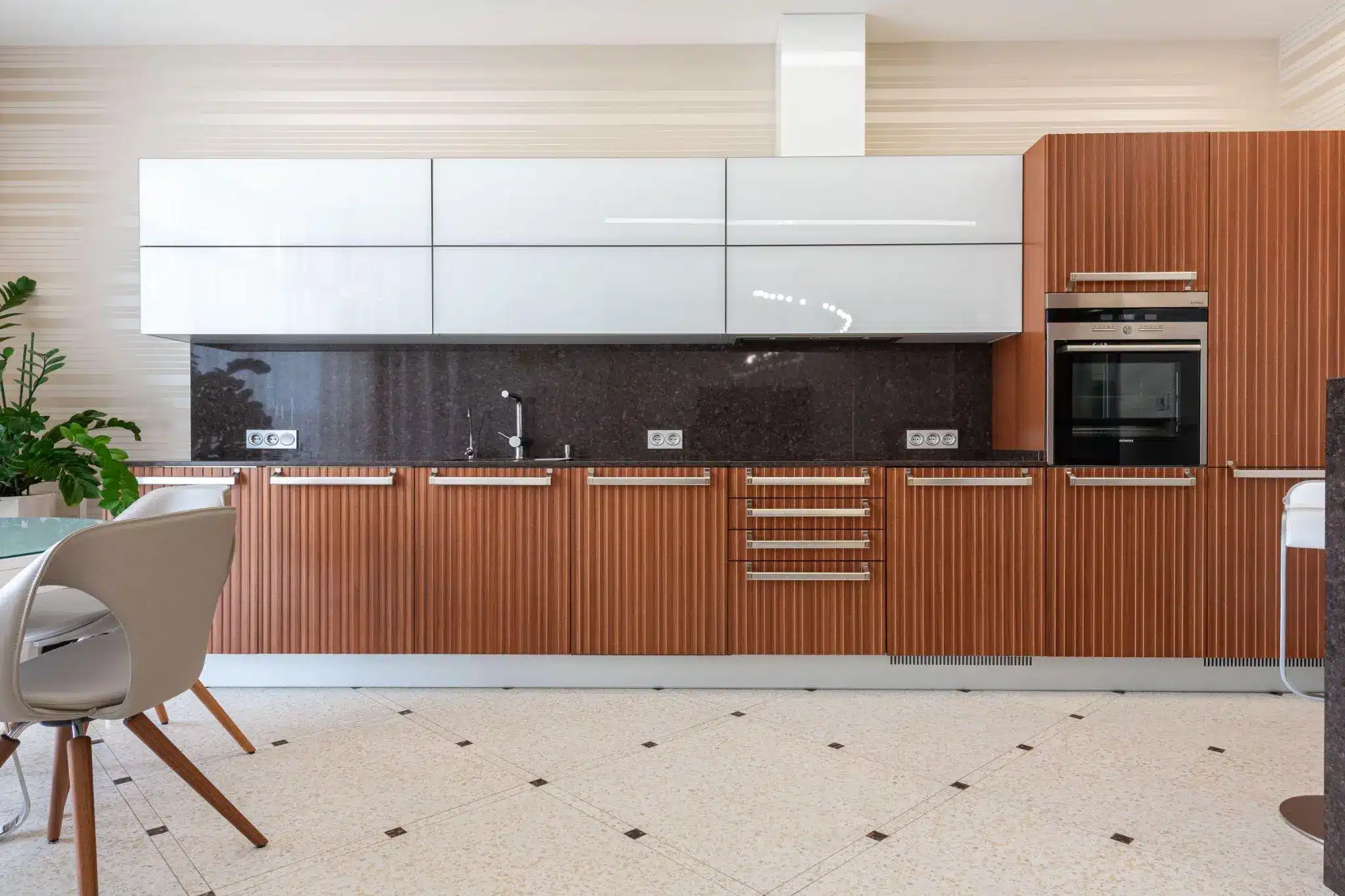 Modern kitchen with wood cabinetry and white accents, featuring built-in oven and sleek marble countertop