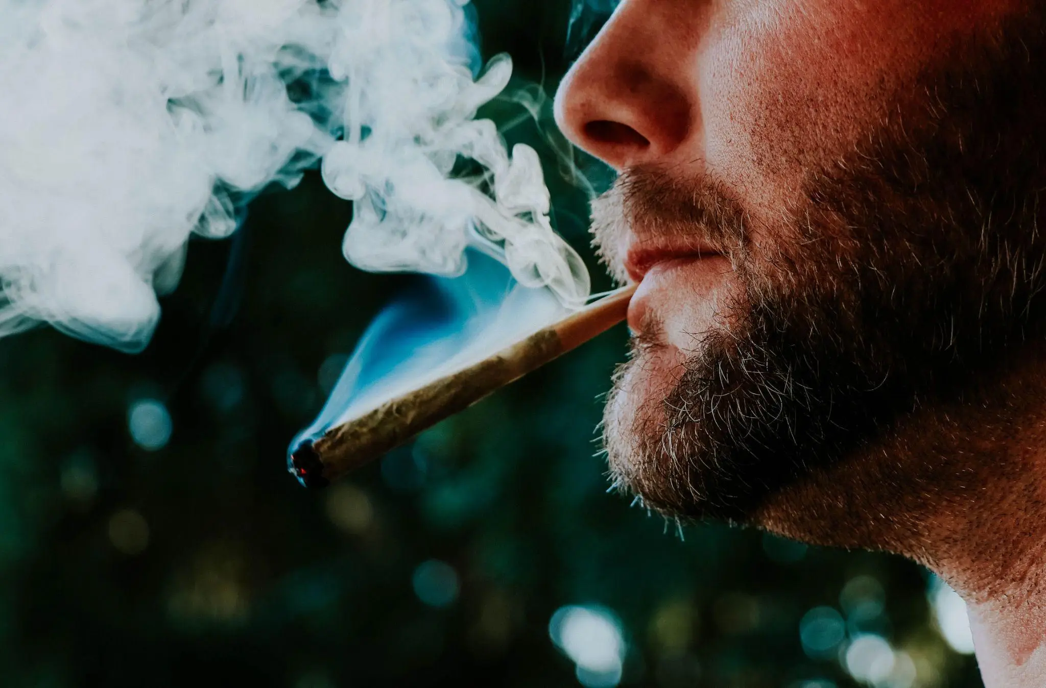 Man smoking a cigar outdoors with smoke swirling around in natural light