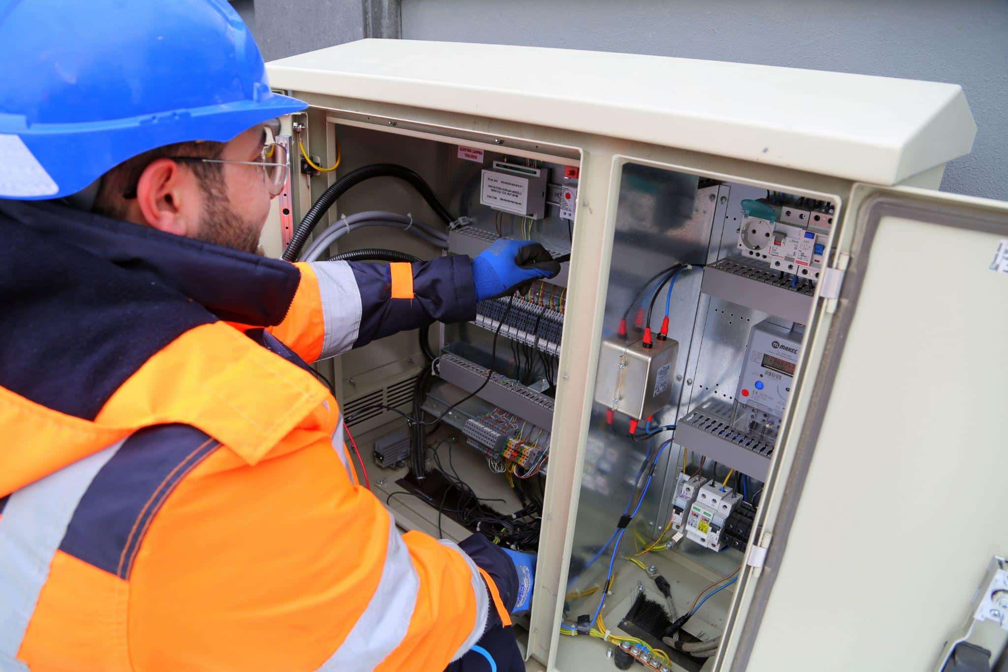 Technician in orange safety gear inspecting electrical control panel outdoors