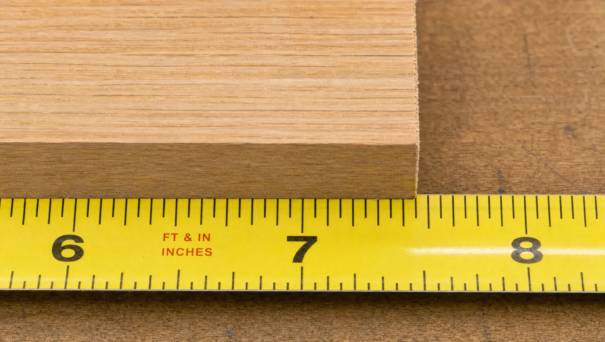 Yellow tape measure showing 6, 7, and 8-inch marks beneath a wooden board to demonstrate reading whole inches.
