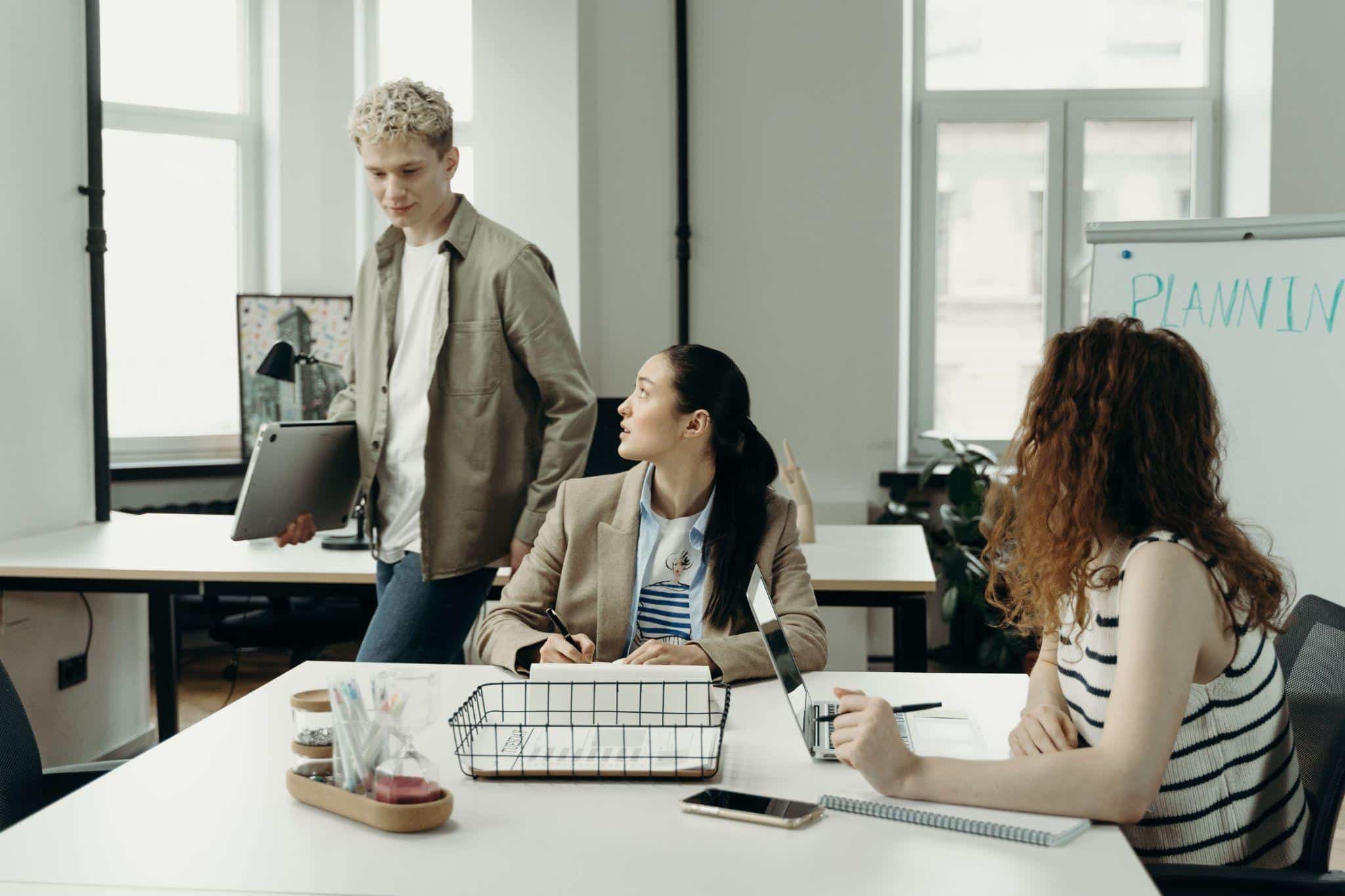 Three people collaborating in a modern office with laptops and whiteboard saying "Planning"