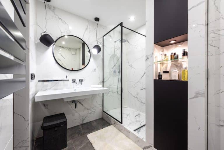 Modern bathroom with marble walls, round mirror, and glass shower enclosure