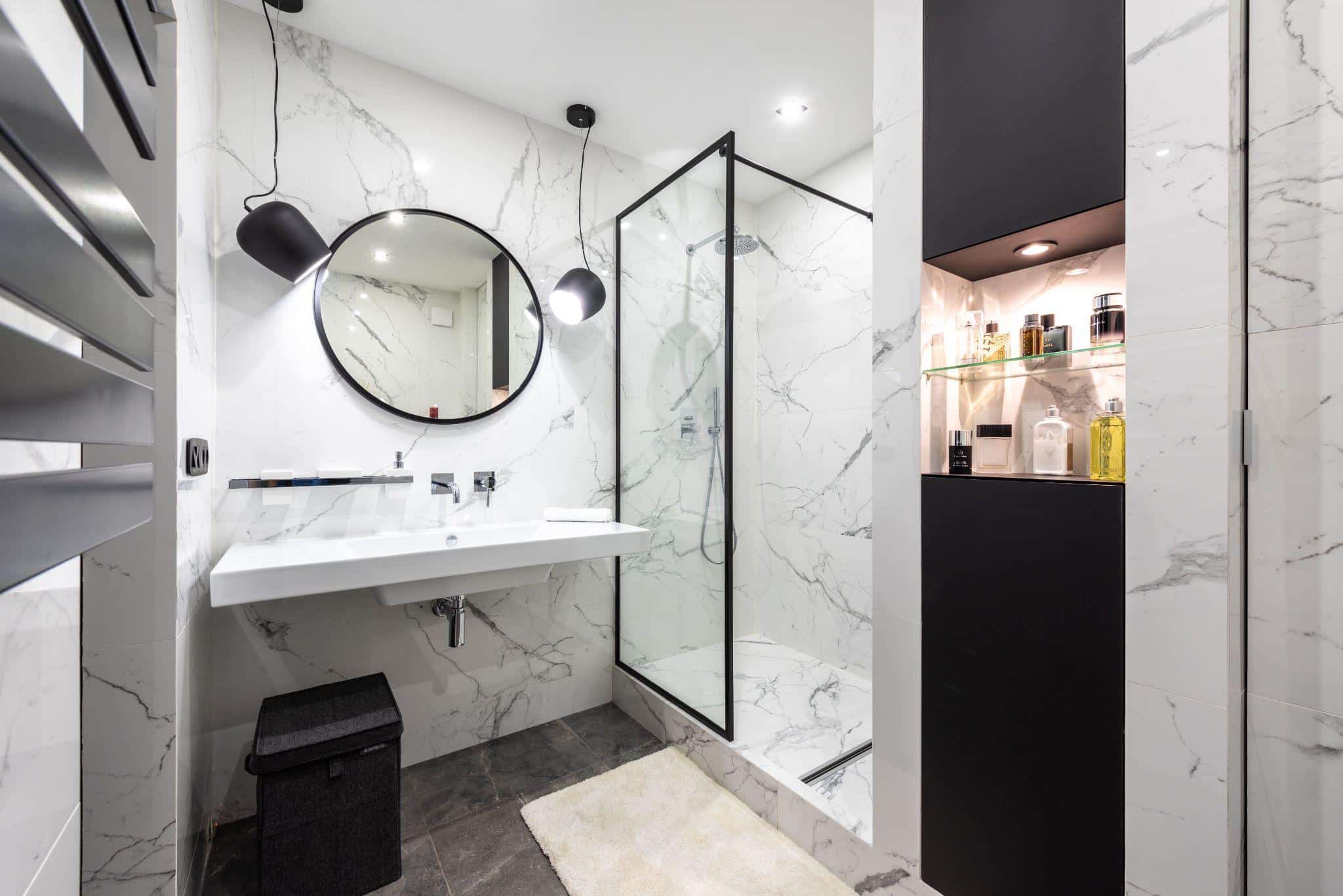 Modern bathroom with marble walls, round mirror, and glass shower enclosure