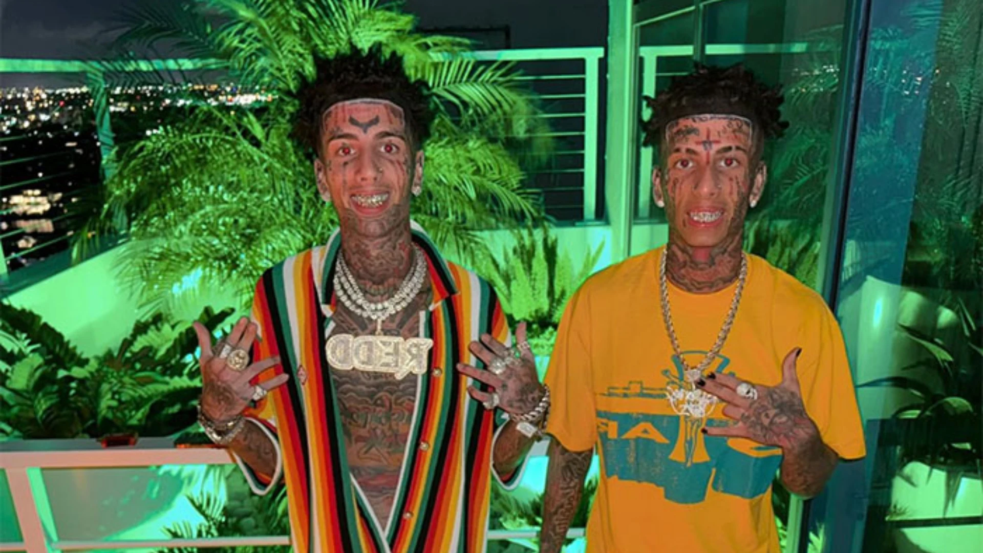 The Island Boys wearing colorful outfits and jewelry while posing together on a balcony at night.