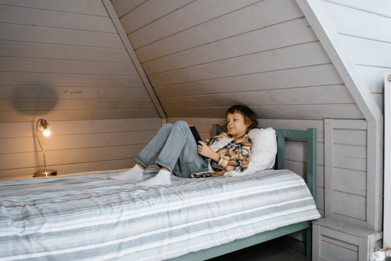 Child using a tablet on a bed in a cozy attic bedroom