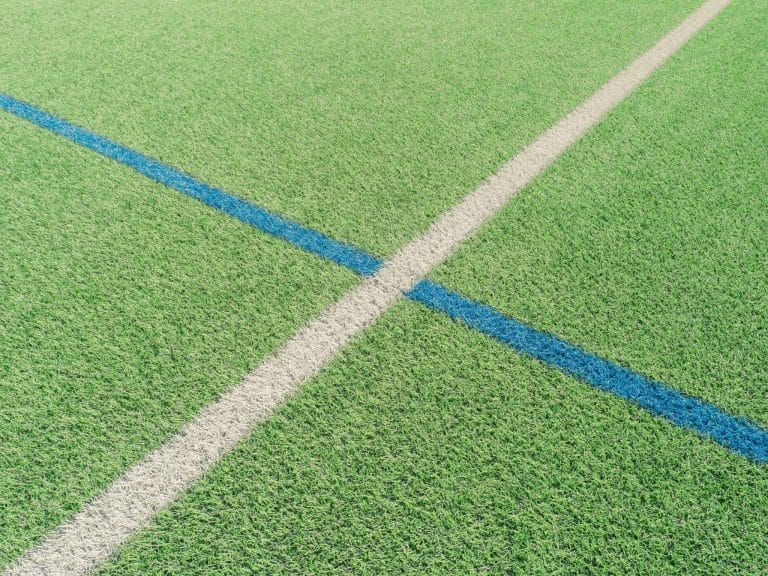 Green sports field with intersecting white and blue lines in bright sunlight